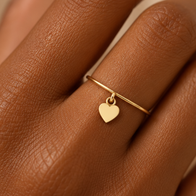 Bague breloque cœur en or jaune 18K portée sur main foncée